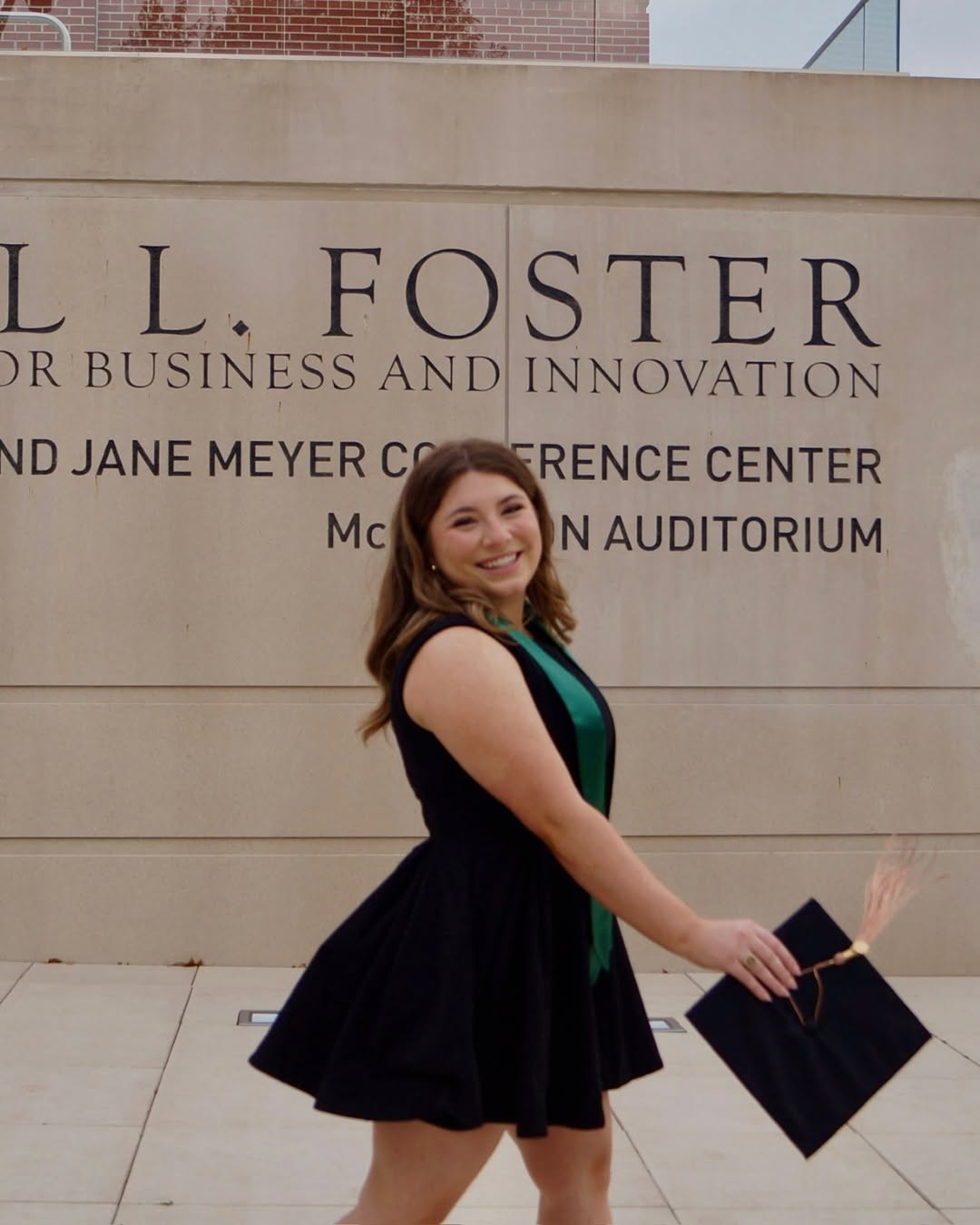Anna Johnson stands outside of the Paul L. Foster business school posing with graduation cap