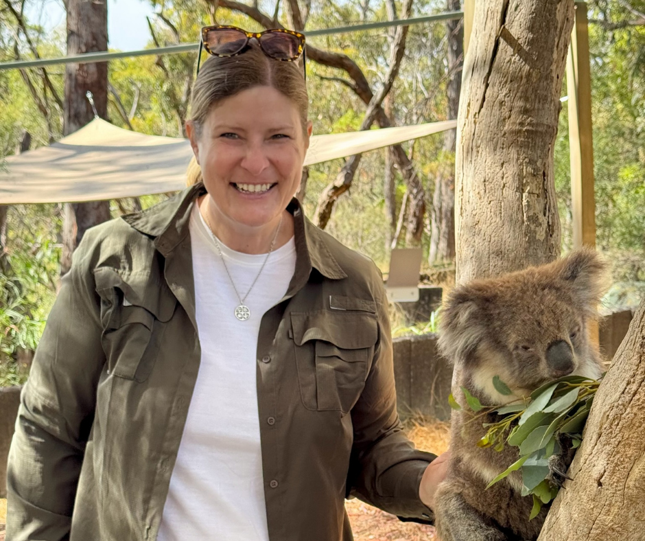 Woman standing next to a feeding koala bear