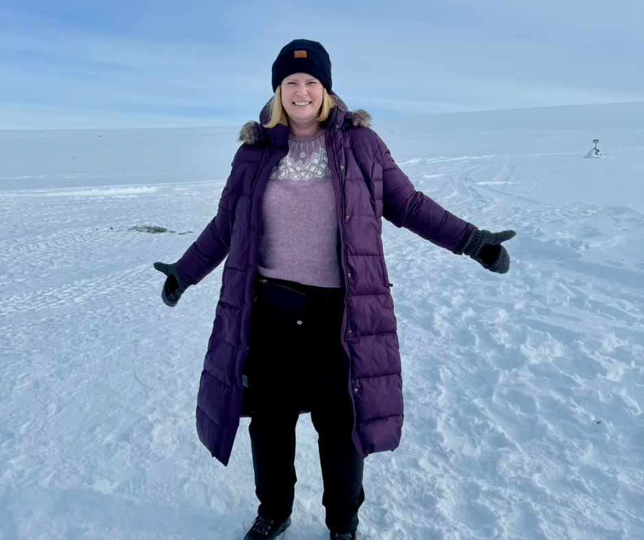 A woman standing in a long puffer coat with a beanie on top of a snowy land