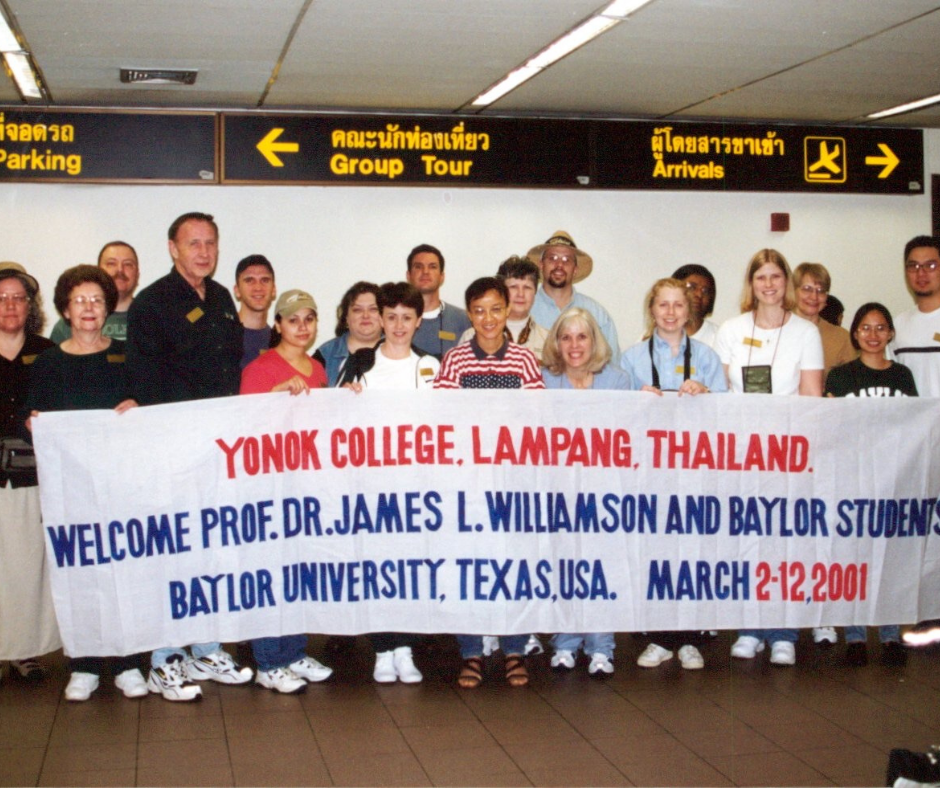 A group of people standing behind a sign that says Laampang Thailand
