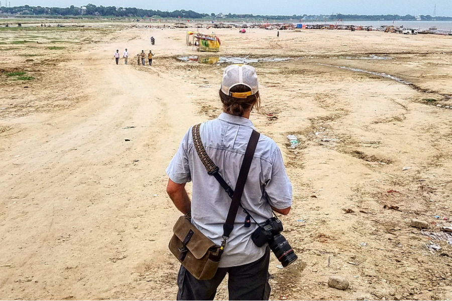 Greg Davis looks out on a dry landscape during one of his international photo trips with a camera strapped to his back.