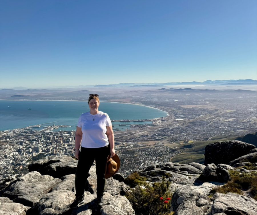 Woman in white t shirt stands on a mountain above the coastline