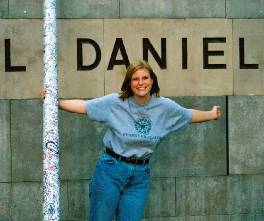 Blonde girl standing outside of a cement building in a gray t shirt and blue jeans